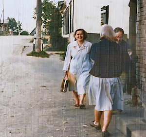 Aglonas Street in Vishki.  Tanya Dumesh has a handbag and is wearing a nurse's uniform.  The hospital, which is the white stone building behind her, was Boris Usdin's house.